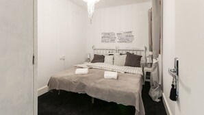 A neatly made bed with a striped bedspread and pillows, a chandelier, a word cloud on the wall, and a striped curtain. - Samba - Apartment In Gandia (Gandia, Valencia)