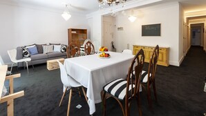 A dining area with a white table, wooden chairs, and a chandelier. There is a sofa and a wooden cabinet in the background. - Samba - Apartment In Gandia (Gandia, Valencia)
