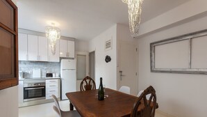 A dining area with a wooden table and chairs, a bottle of wine, and a clock on the wall. - Samba - Apartment In Gandia (Gandia, Valencia)