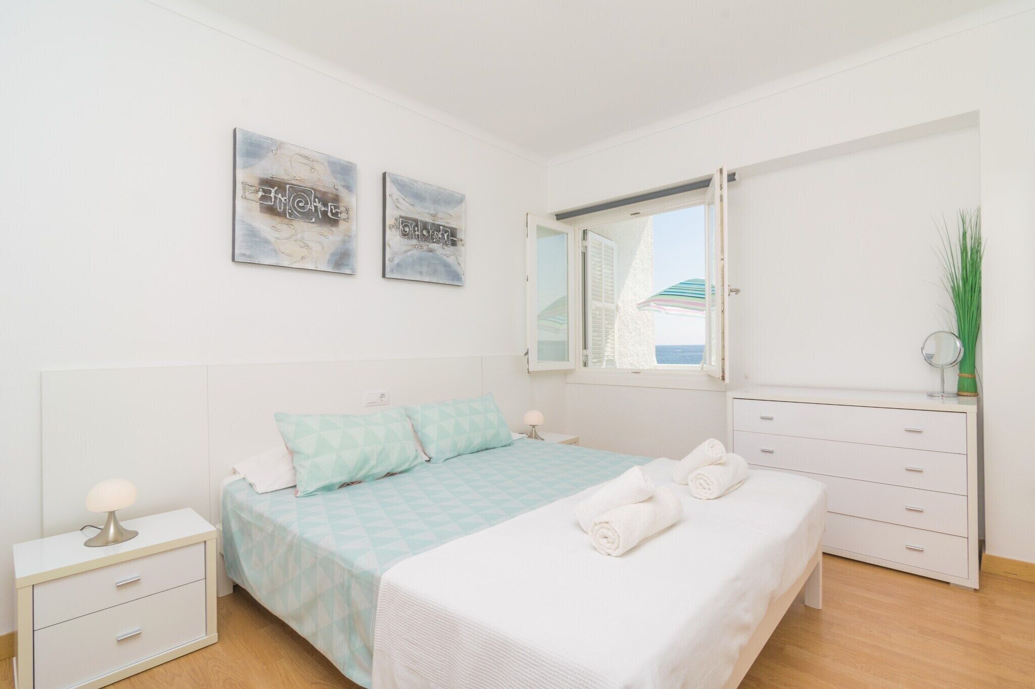 A bedroom with a bed, bedside tables, a dresser, a mirror, and artwork on the wall.