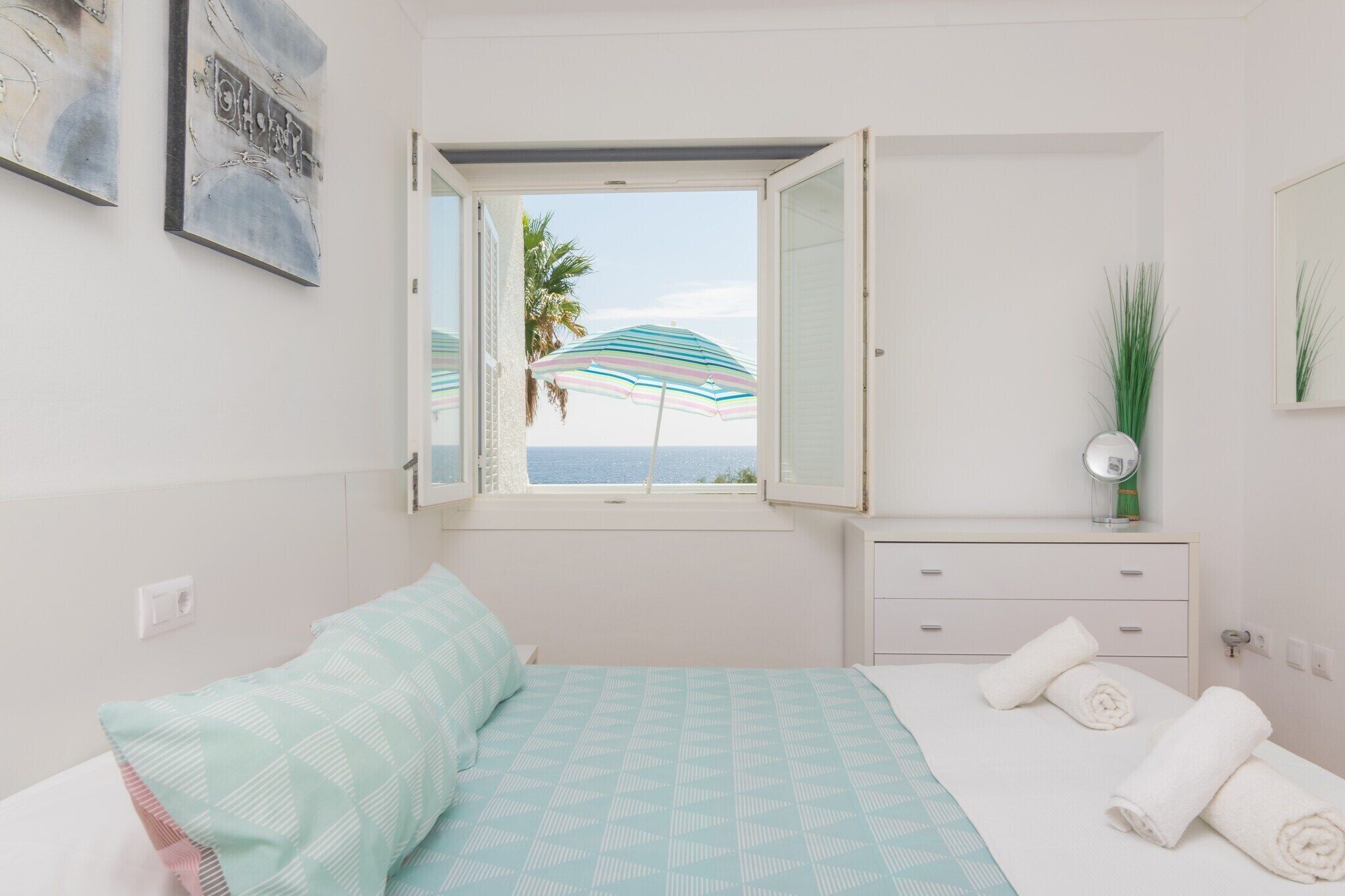 Quarto com cama, cômoda, janela com vista e espelho.