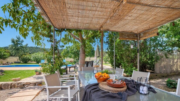 An outdoor dining area with a glass table, white chairs, and a woven shade. - Can Sua - Villa With Private Pool In Artà (Artà, Illes Balears)
