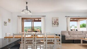 Ein modernes Wohnzimmer mit Essbereich, großen Fenstern und Blick auf Grünflächen.