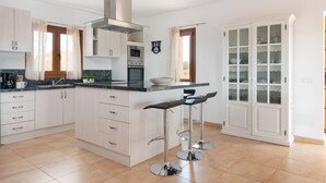 Eine moderne Küche mit weißen Schränken, einer Edelstahl-Dunstabzugshaube, einer Mikrowelle und einem Backofen. Zwei Barhocker und ein Fenster mit Vorhängen sind ebenfalls vorhanden.