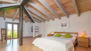 A bedroom with a large bed, wooden floor, a ceiling with exposed beams, a window, and a radiator. - Can Ribas - Villa With Private Pool. Free Wifi (Can Picafort, Illes Balears)