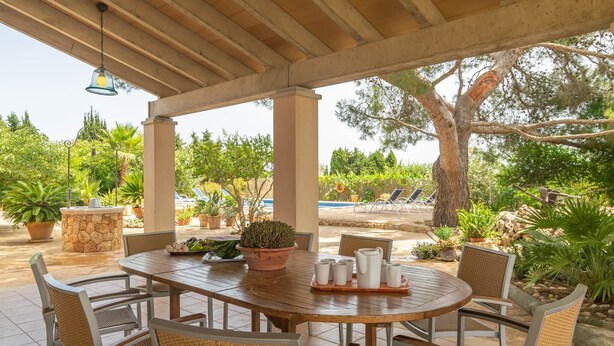 An outdoor patio with a round wooden table, wicker chairs, and potted plants. - Can Ribas - Villa With Private Pool. Free Wifi (Can Picafort, Illes Balears)