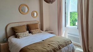 A bedroom with a bed, two wall mirrors, a bedside table, a hanging light fixture, and a window with curtains. - Beautiful renovated village house in the heart of Provence. (Graveson)