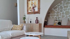 A cozy living room with a sofa, two white round tables, a woven rug, a stone wall, and a painting on the wall. - Beautiful renovated village house in the heart of Provence. (Graveson)