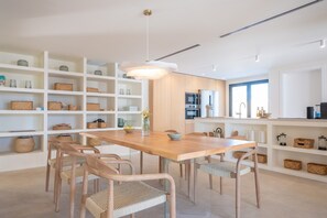 A modern kitchen with white cabinetry, a wooden dining table, wicker chairs, and a pendant light.