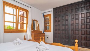 Ein Hotelzimmer mit einem Bett, zwei zusammengerollten Handtüchern, einer Holzkommode, einem Spiegel und einer großen, dunklen Holztür.