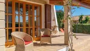 Ein überdachter Patio-Bereich mit Korbstühlen und einer Glastür, die zu einem Poolbereich führt.
