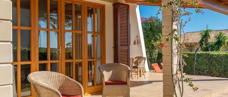 A covered patio area with wicker chairs and a glass door leading to a pool area.