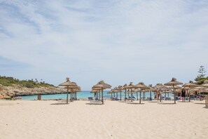 Ein Strand mit Reetdachschirmen und Liegestühlen.