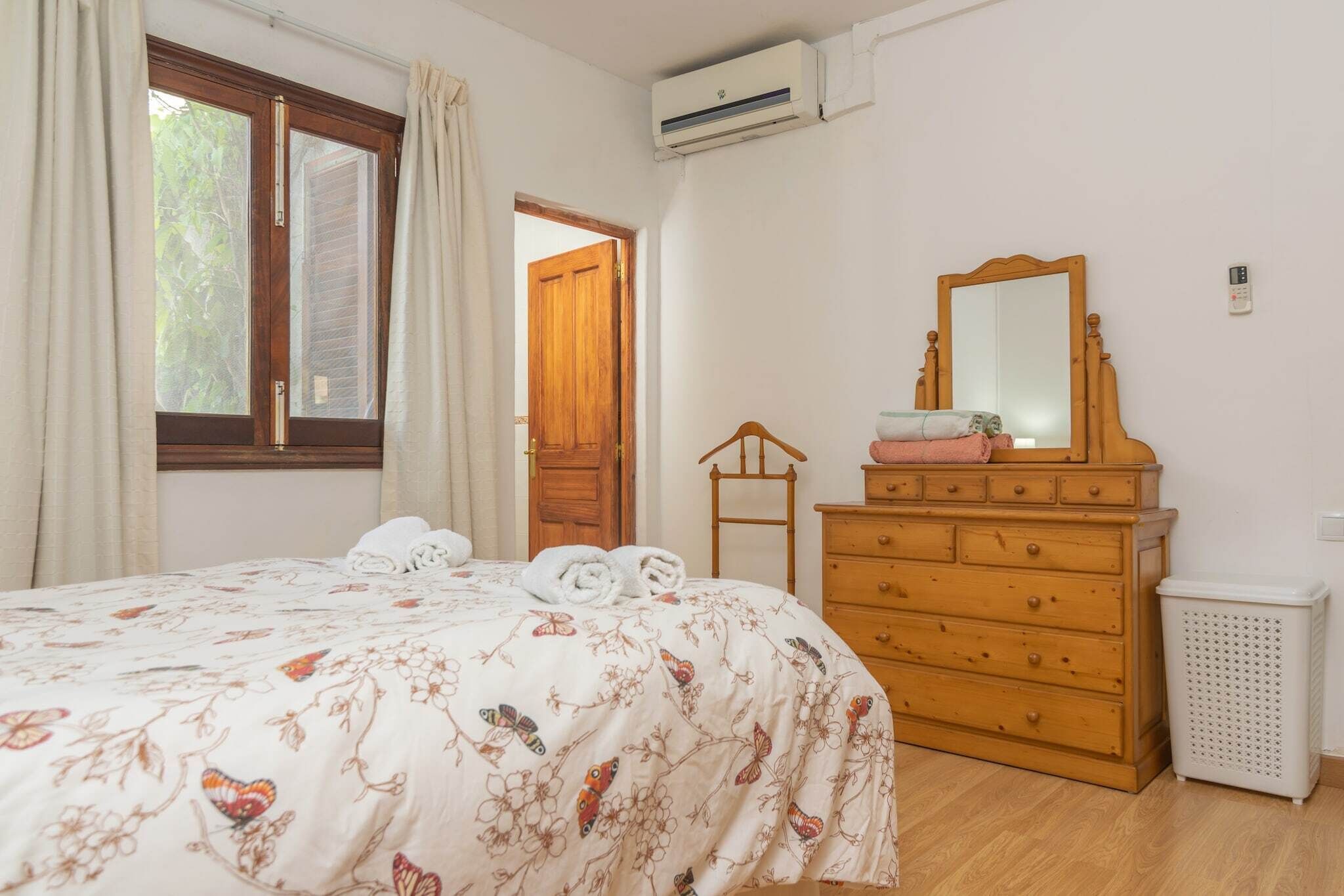Een slaapkamer met een bed, een dressoir, een spiegel en een raam met gordijnen.