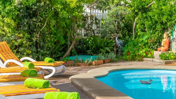 A poolside area with lounge chairs and towels, surrounded by lush greenery and a Buddha statue.