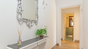 A hallway with a white wall, a decorative mirror, a small plant, and a vase with reed sticks.