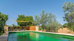 A rectangular swimming pool with clear green water, surrounded by a wooden fence and trees.