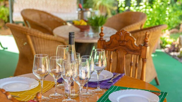 A table set with wine glasses and plates, surrounded by wicker chairs.