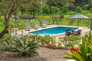 A swimming pool with lounge chairs and a table, surrounded by greenery and rocks.