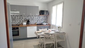 A compact kitchen with grey cabinets, a microwave, a sink, and a dining table set for two.