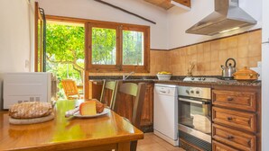 A kitchen with a wooden table, a white dishwasher, an oven, and a window with a view of greenery.