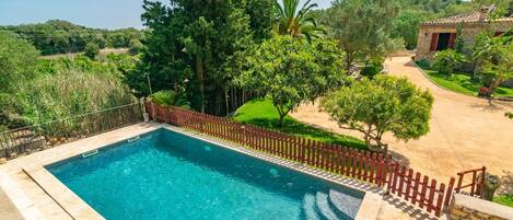 A swimming pool with a stone border, surrounded by a wooden fence and lush greenery.