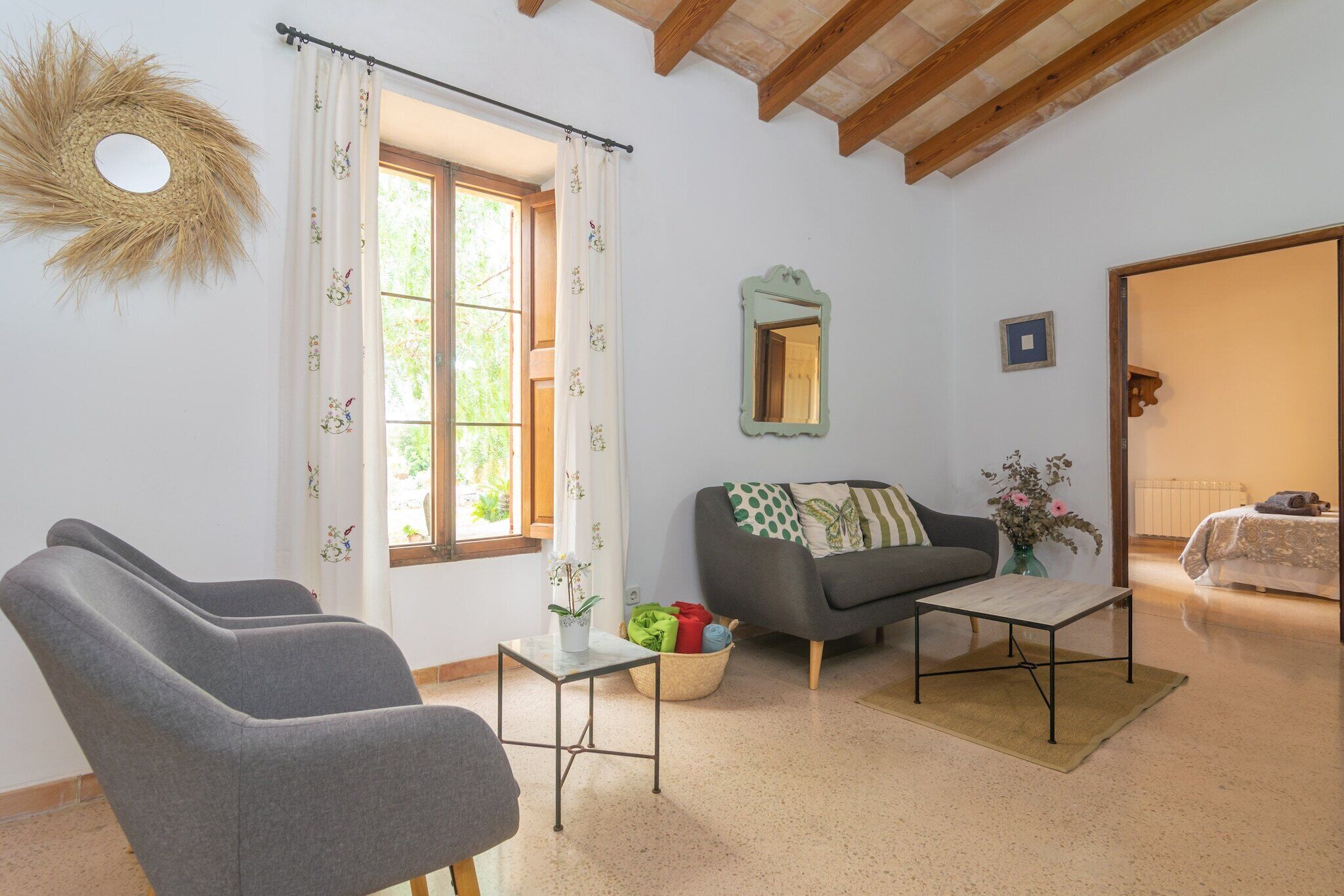 Ein Wohnzimmer mit einer Couch, zwei Sesseln, einem kleinen Tisch, einem Spiegel und einem Fenster mit Vorhängen.