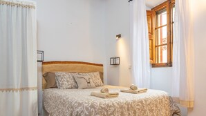 A neatly made bed with a patterned bedspread and two pillows, a bedside lamp, and a window with curtains.