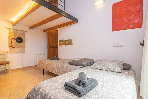 Un dormitorio con dos camas, un banco de madera, una lámpara de pared y un tapiz rojo estampado.