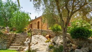 A stone staircase leading to a rustic building with a tiled roof, surrounded by lush greenery and trees.