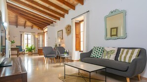 A spacious living room with a wooden ceiling, a grey sofa with patterned cushions, a coffee table, and a mirror on the wall.