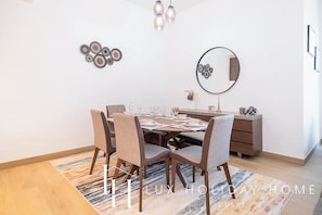 A modern dining area with a round table set for four, surrounded by upholstered chairs. There is a wooden cabinet with decorative items and a mirror on the wall. - LUX The Elegant Sea View Suite (Dubai)