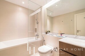 A modern bathroom with a glass-enclosed shower, a freestanding bathtub, a toilet, and a vanity with a marble countertop. - LUX The Elegant Sea View Suite (Dubai)