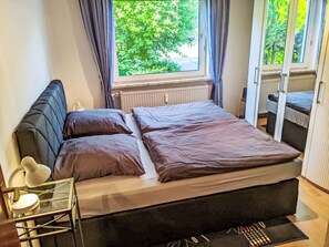 A bedroom with a bed, a nightstand, a lamp, and a view of greenery outside. - Harzsonne by Interhome (Clausthal - Zellerfeld)