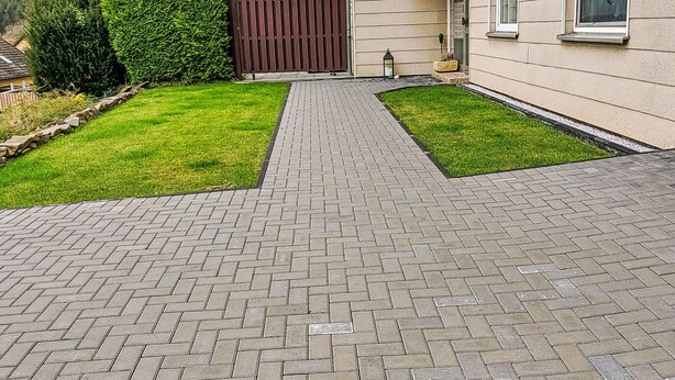 Un camí pavimentat que condueix a una casa amb tanca de fusta i un petit jardí.