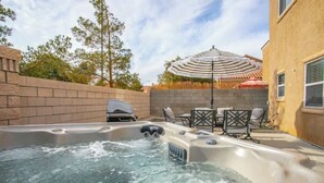 Un bain à remous avec un barbecue et du mobilier d’extérieur, le tout entouré d’un mur de briques et d’arbres.