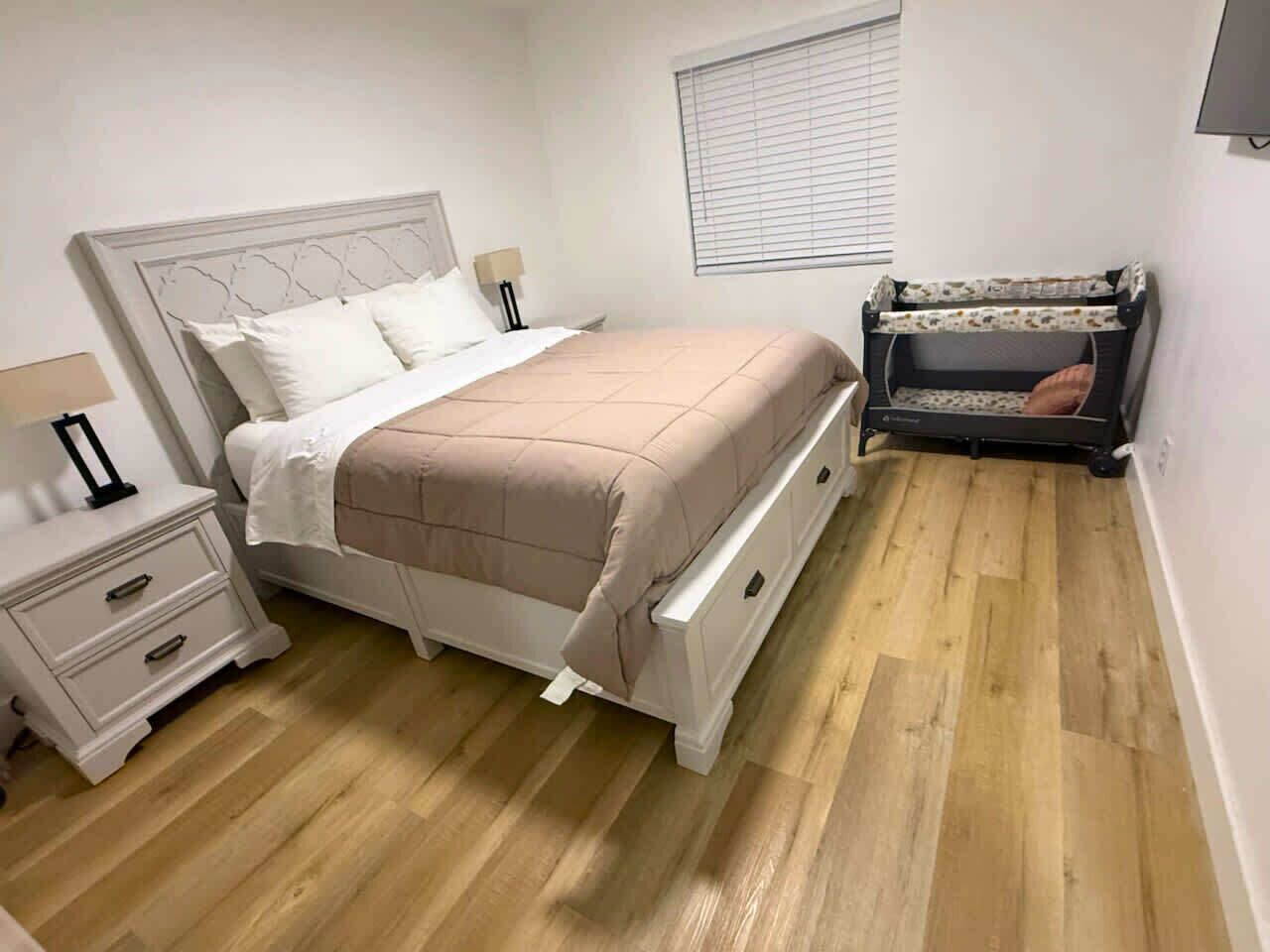 Un dormitorio con cama, mesita de noche, cuna y ventana.