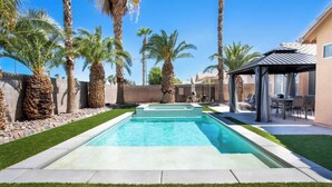 Une piscine rectangulaire à l’eau d’un bleu limpide, entourée de pelouse bien entretenue et de palmiers.