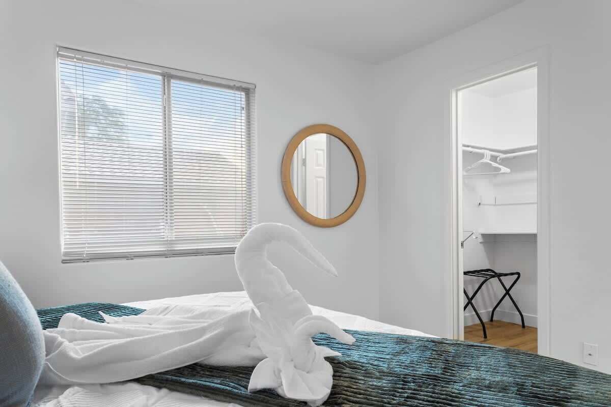 Een slaapkamer met een bed, een raam met zonwering, een spiegel en een inloopkast.