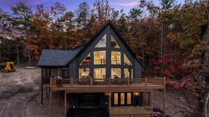 A modern two-story cabin with a balcony, surrounded by autumn foliage.