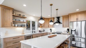 A modern kitchen with wooden cabinets, a large island, stainless steel appliances, and pendant lighting.