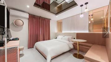 A modern hotel room with a large bed, a desk with a computer, a round mirror, and a small table.