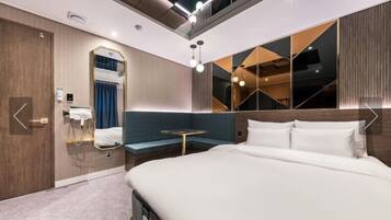 A modern hotel room with a large bed, a seating area, a mirror, and a small table.