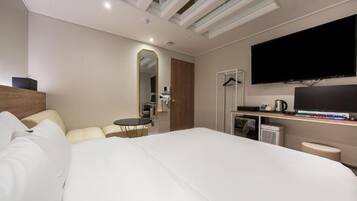 A modern hotel room with a large bed, a desk with a computer, a flat-screen TV, and a small seating area.