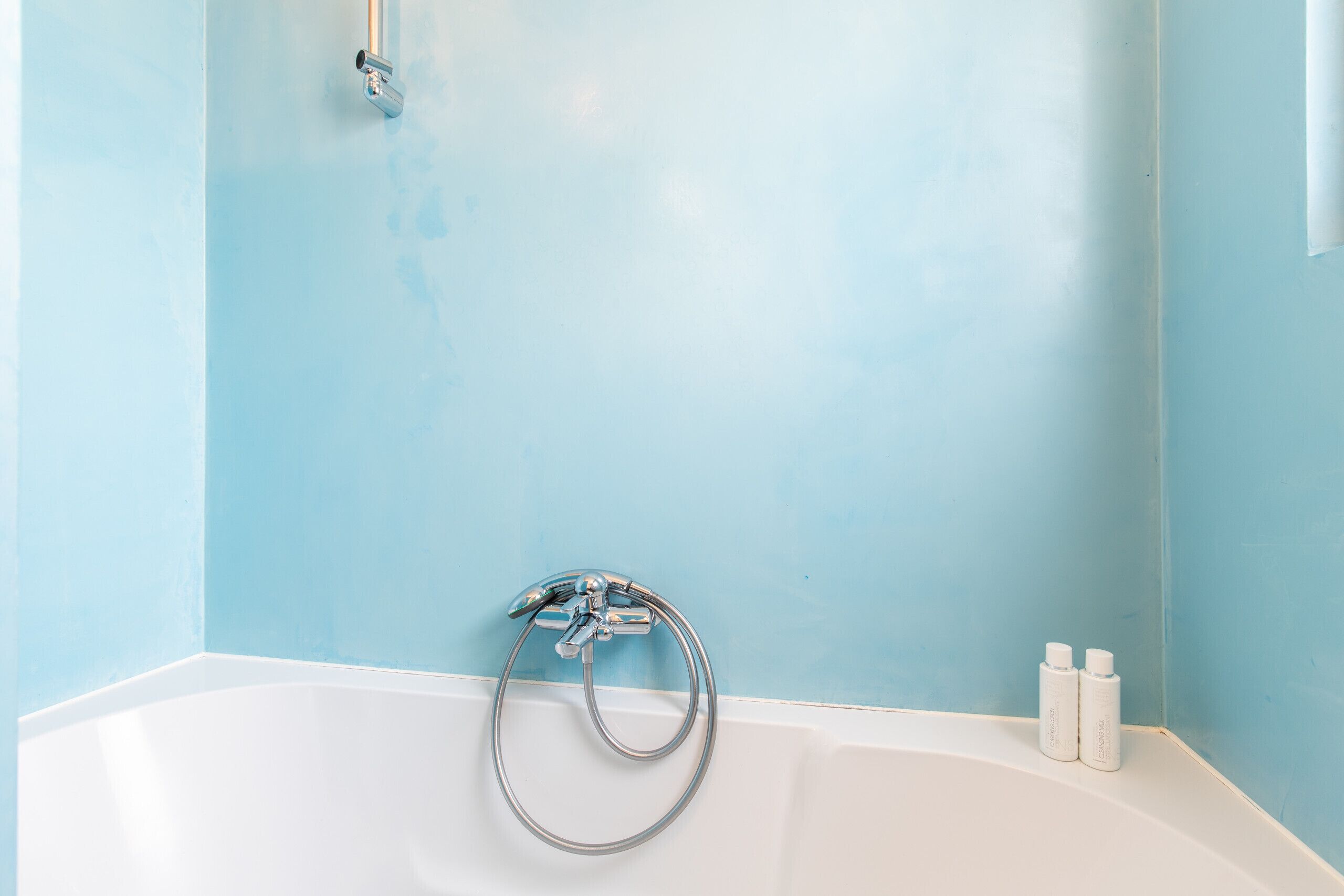 A bathroom with a bathtub, a shower head, and two bottles of shampoo.