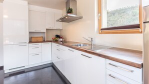 A modern kitchen with white cabinets, a wooden countertop, a stainless steel sink, and a window with a view of greenery.