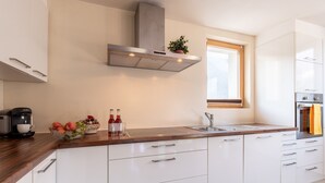 A modern kitchen with white cabinets, a stainless steel range hood, a window, and a countertop with a coffee maker and fruit bowl.