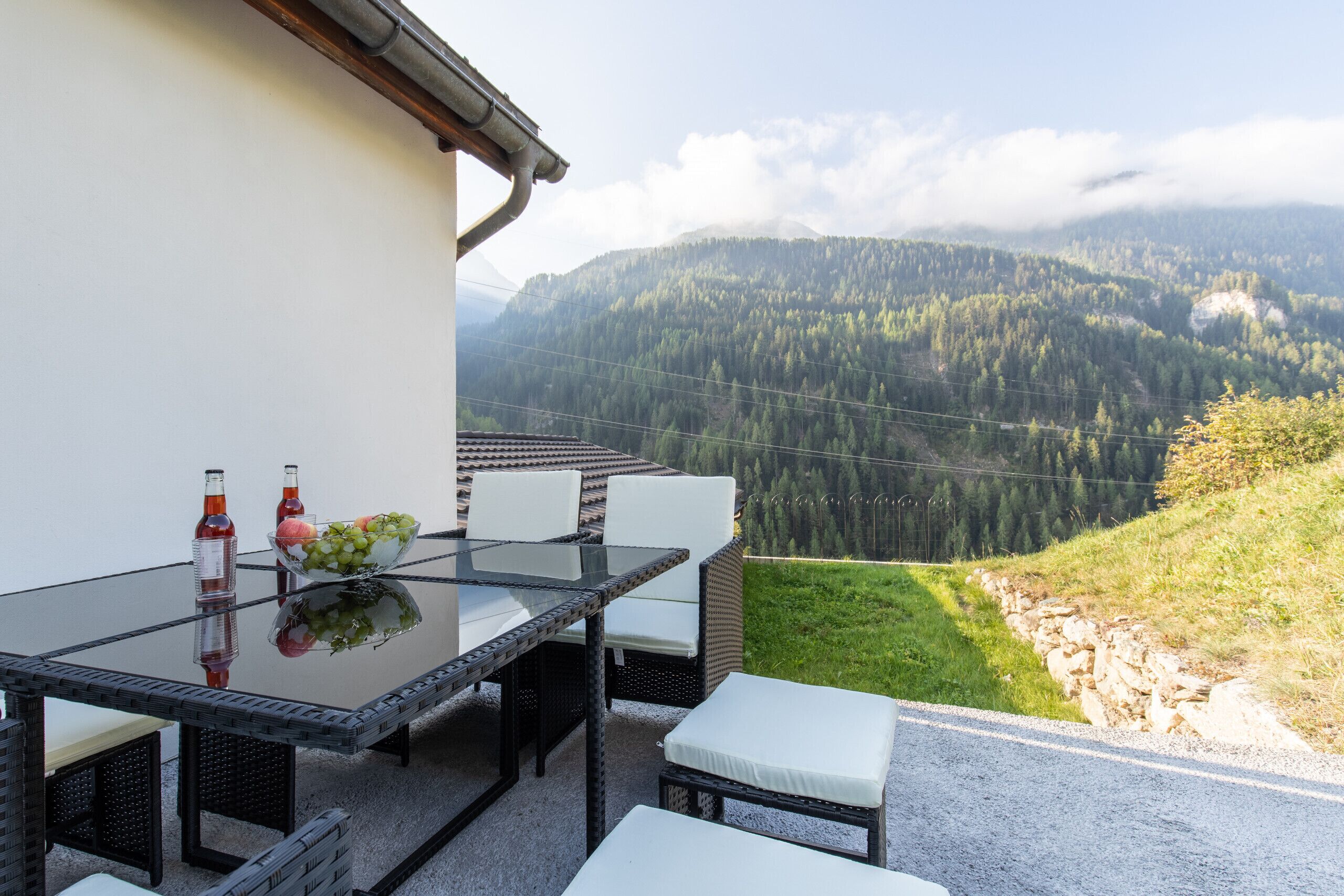 Un espace repas avec une table en verre et des chaises blanches, donnant sur un paysage montagneux.