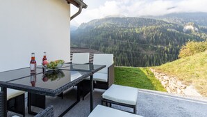 A dining area with a glass table and white chairs, overlooking a mountainous landscape.