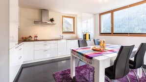 A modern kitchen with white cabinets, a wooden countertop, and a window overlooking a forest.